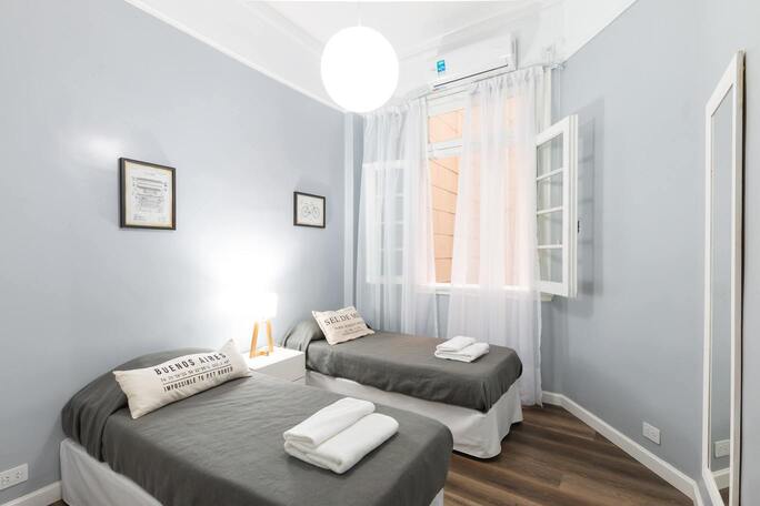 Une chambre d'hôtel avec deux lits simples, des murs bleu clair et une fenêtre.